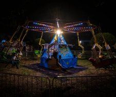 A carnival ride is lit up at night and people are riding it.