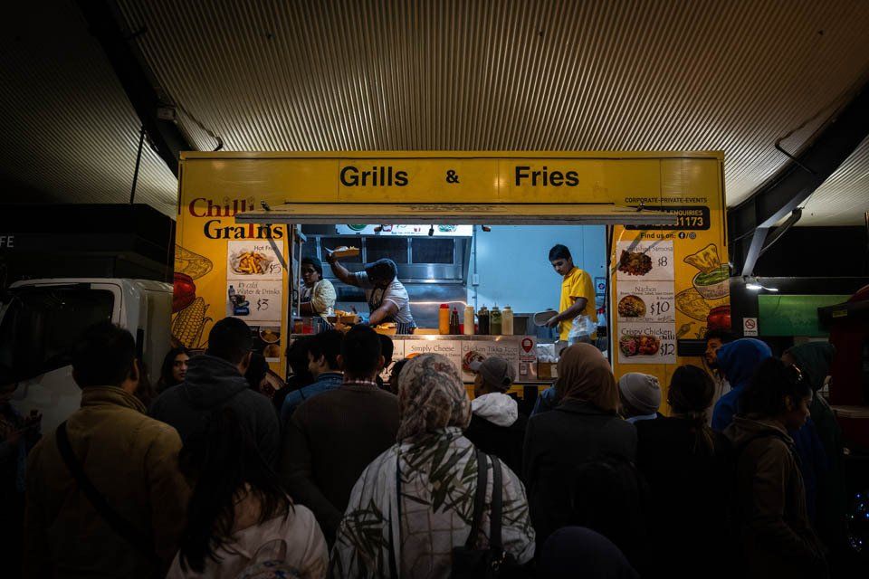 A crowd of people are standing outside of a food truck.