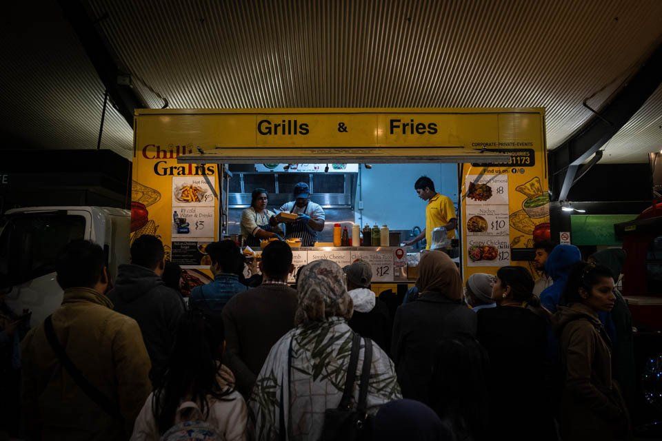 A crowd of people are standing in front of a food truck.