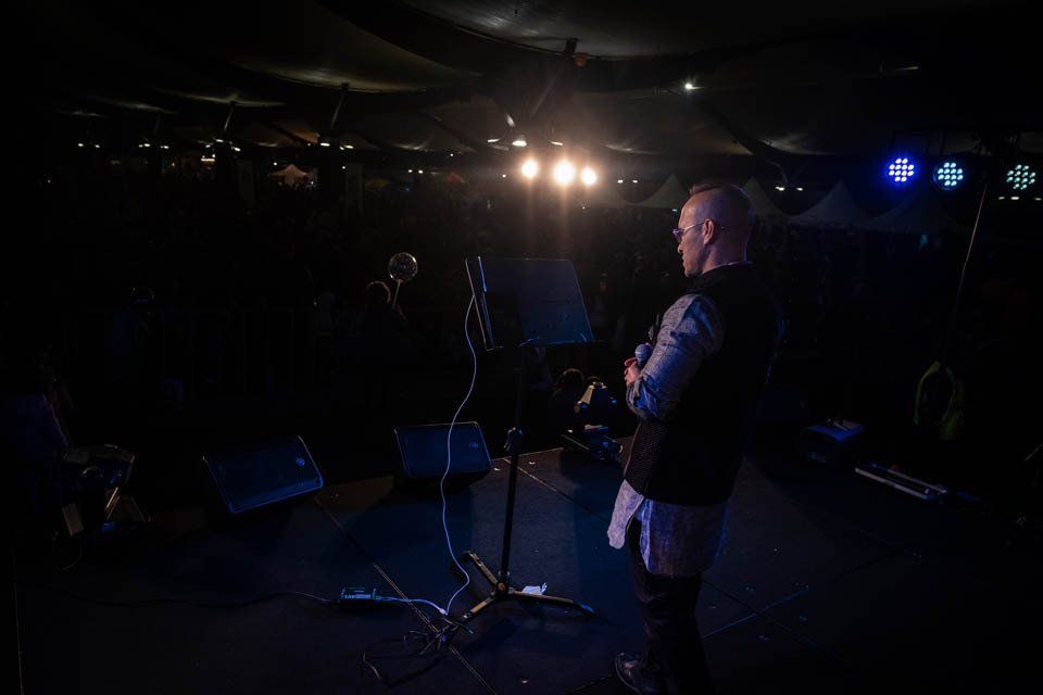 A man is standing on a stage playing a guitar in front of a crowd.