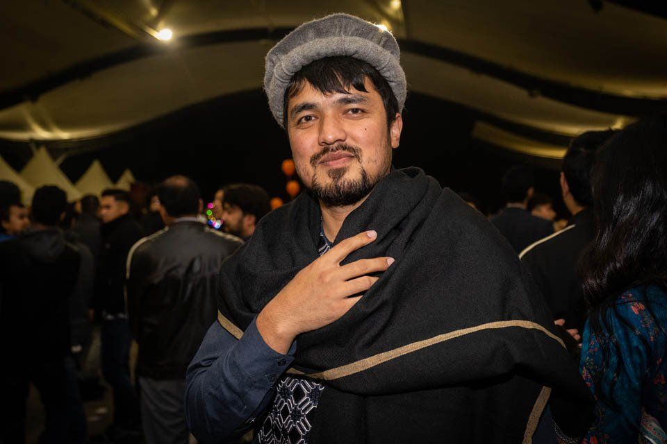 A man wearing a hat and a scarf is standing in a crowd of people.