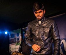 A man in a black leather jacket is standing in a dark room.