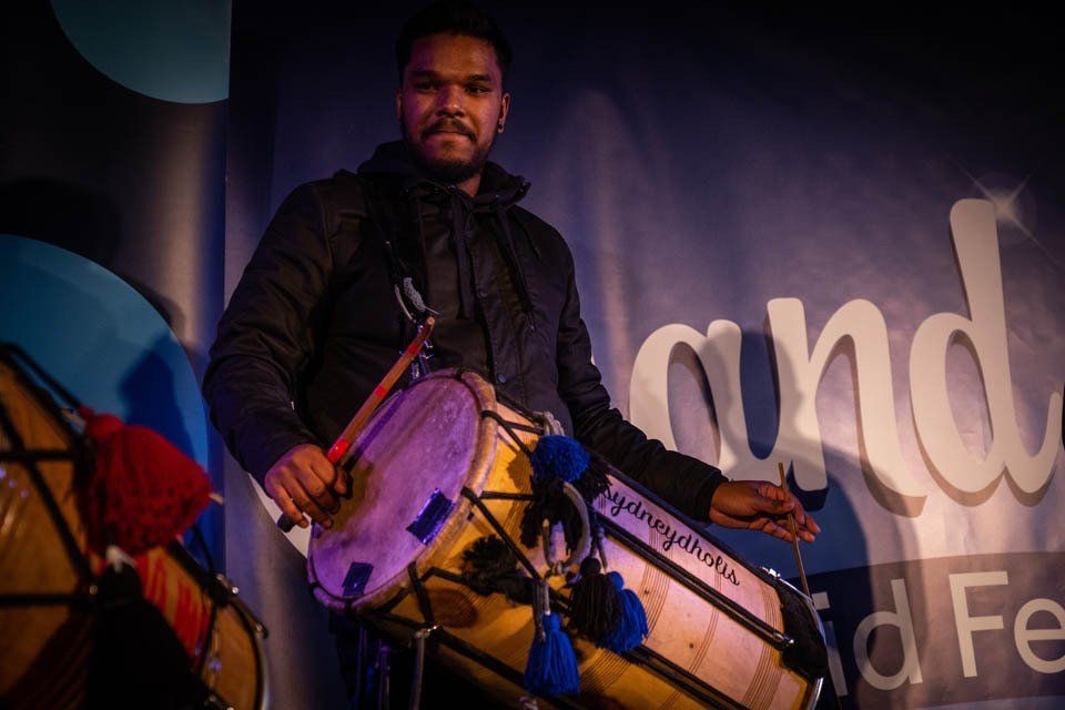 A man is playing a drum in front of a sign that says and.