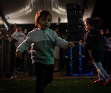 A group of children are dancing in a tent at night.