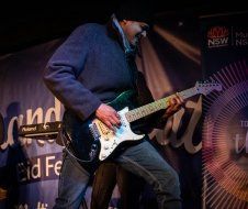 A man is playing a guitar in front of a sign that says nsw
