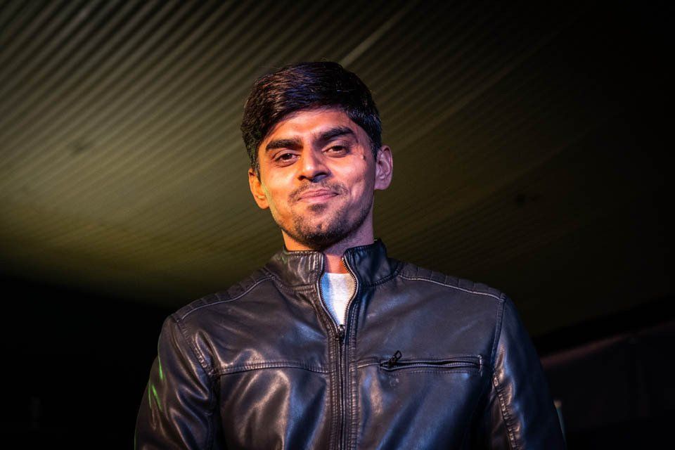 A man in a black leather jacket is smiling in a dark room.