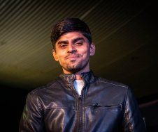 A man in a leather jacket is smiling in a dark room.