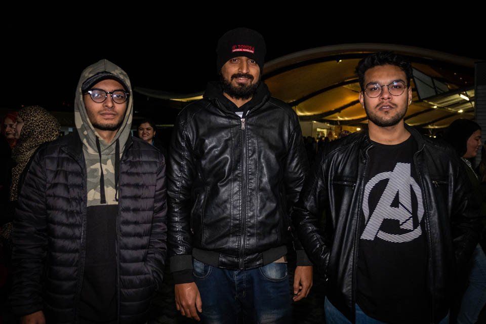 Three young men are standing next to each other in a dark room.