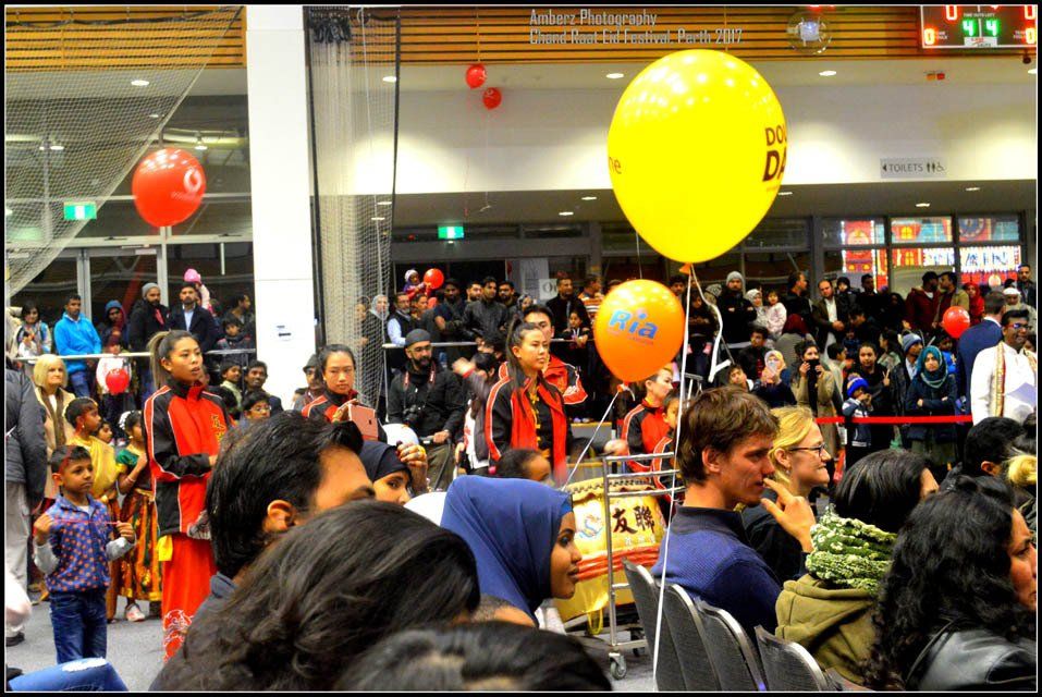 A crowd of people are gathered in front of a building with balloons hanging from the ceiling