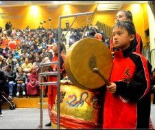 A young boy is playing a drum in front of a crowd.