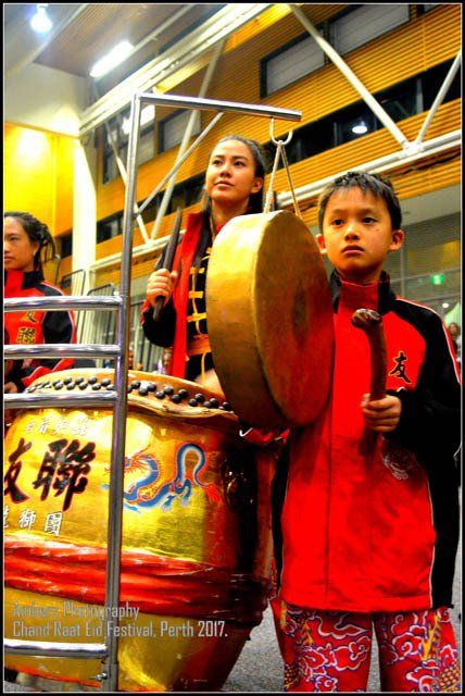 A girl in a red jacket is playing a drum