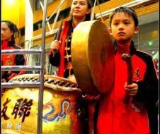 A boy in a red jacket is playing a drum
