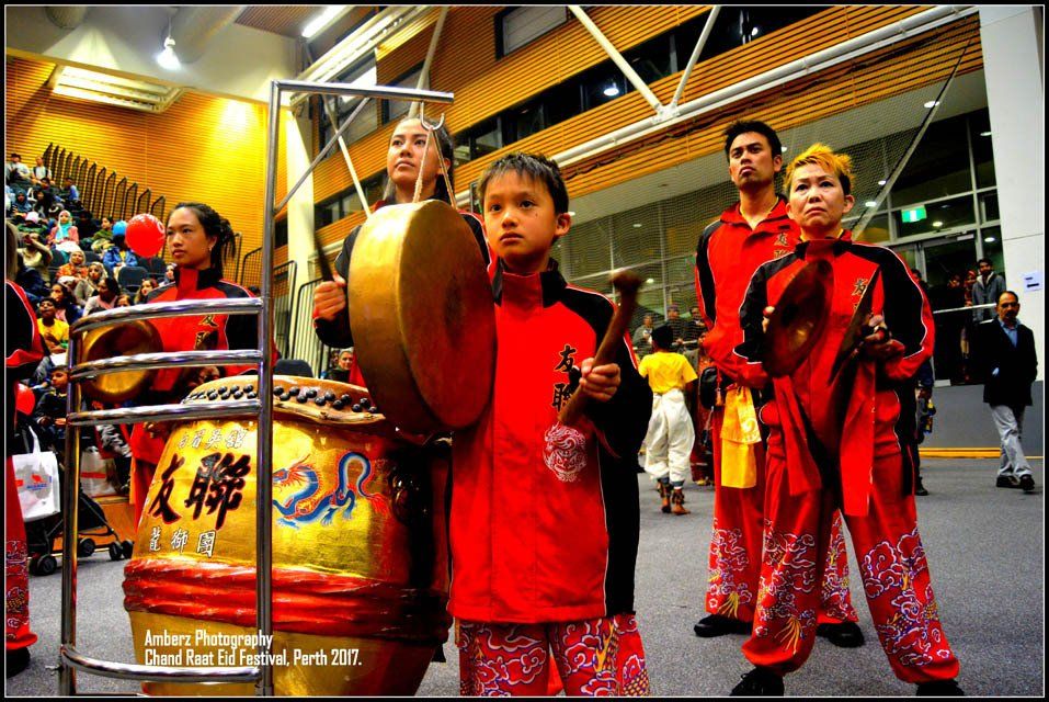 A boy is playing a drum in front of a drum with chinese writing on it