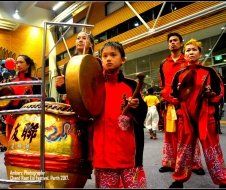 A young girl is playing a drum in front of a group of people.