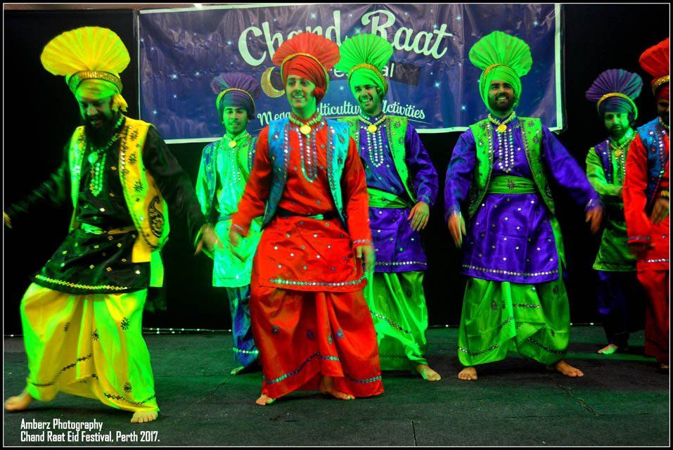 A group of men are dancing in front of a sign that says ' chard raat '