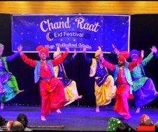 A group of people are dancing in front of a sign that says chand raat eid festival.