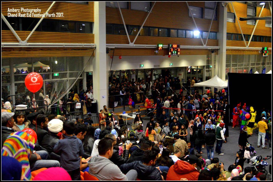 A crowd of people are gathered in a large room with a red balloon that says 6 on it