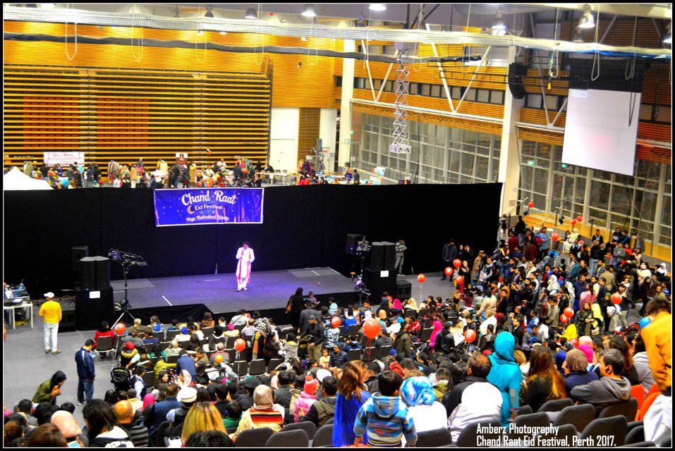 A large crowd of people are gathered in an auditorium watching a man on stage