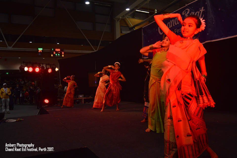 A group of women are dancing on a stage in a dark room.