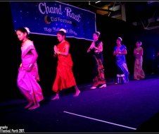 A group of people are dancing on a stage in front of a sign that says chand road.