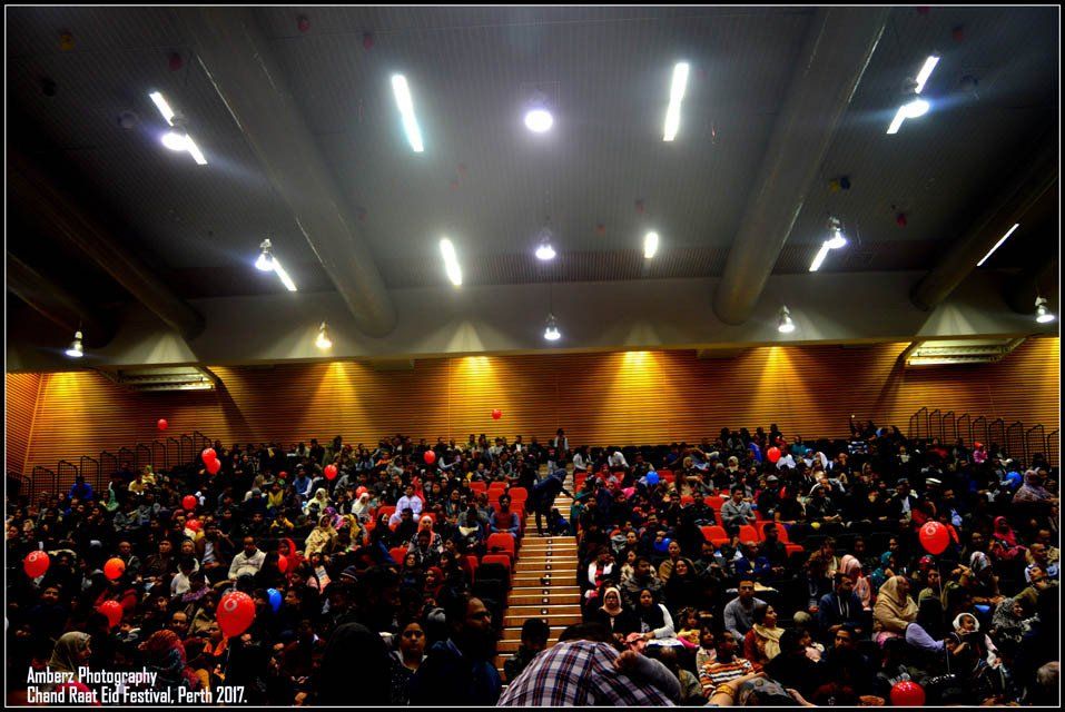A large crowd of people sitting in an auditorium with balloons in the air