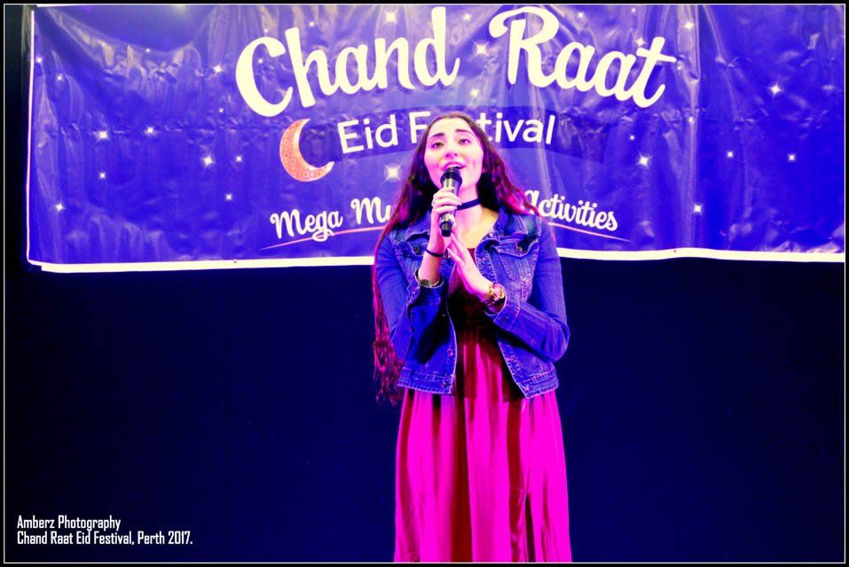 A woman singing into a microphone in front of a banner that says chand raat