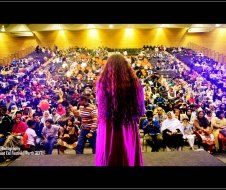 A woman in a purple dress is standing in front of a crowd in an auditorium.