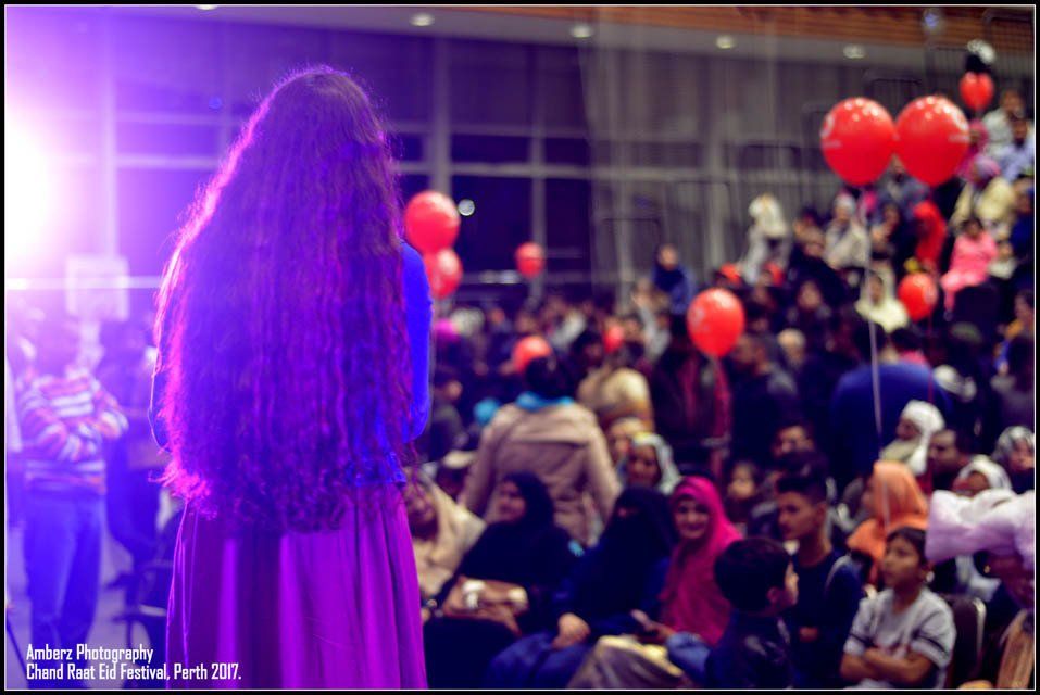 A woman with long hair is standing in front of a crowd with red balloons