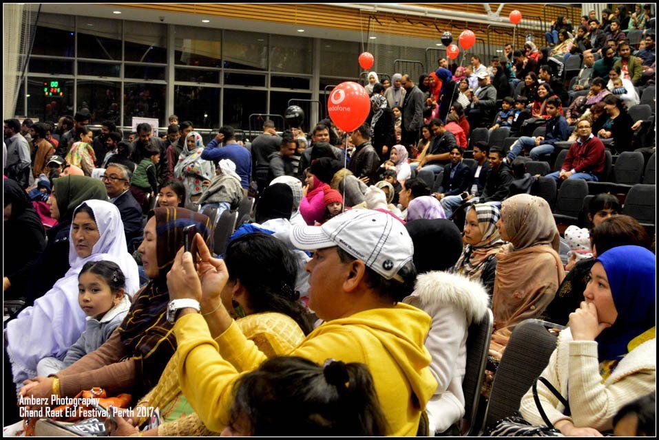 A crowd of people are sitting in a stadium with balloons hanging from the ceiling.