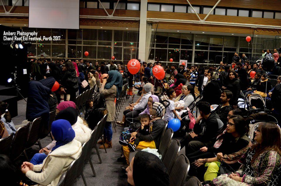 A large group of people are sitting in a room with balloons