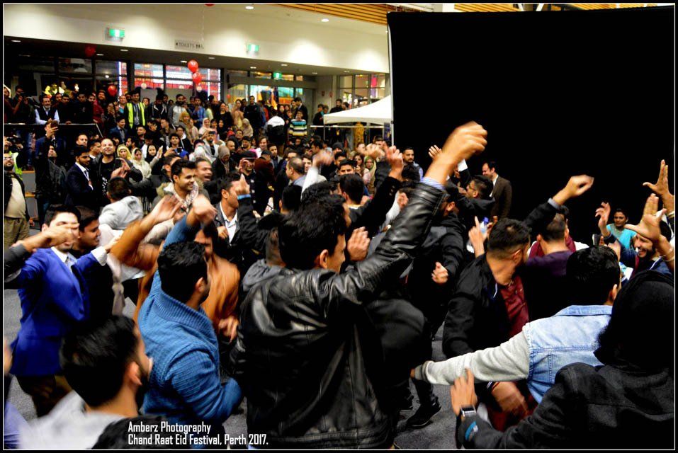 A crowd of people are gathered in a room with their hands in the air