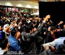 A crowd of people are dancing in a room with their hands in the air.