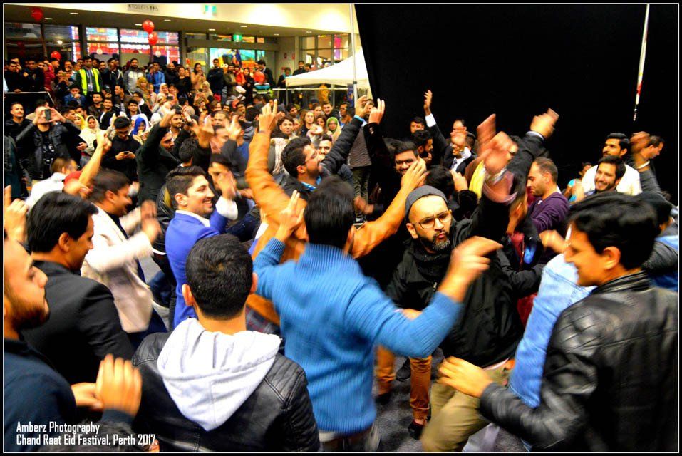 A crowd of people are dancing in a room with their hands in the air