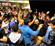 A crowd of people are dancing in a room with their arms in the air.