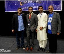 A group of men are posing for a picture in front of a sign that says eid festival.