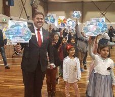 A man in a suit and tie is standing next to a group of children holding up signs.