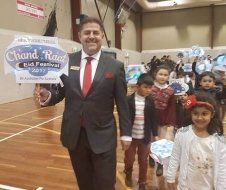 A man in a suit and tie is holding a sign in front of a group of children.