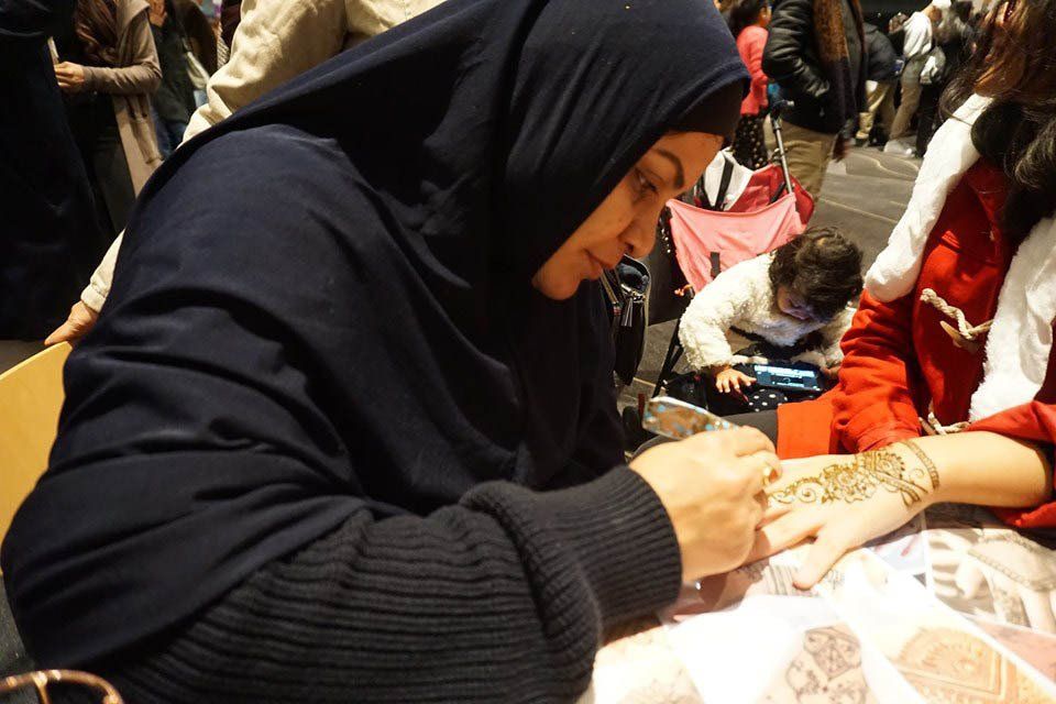 A woman in a hijab is applying henna to another woman 's hand