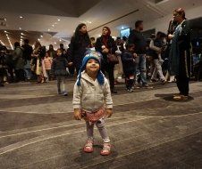 A little girl wearing a hat is standing in front of a crowd of people.