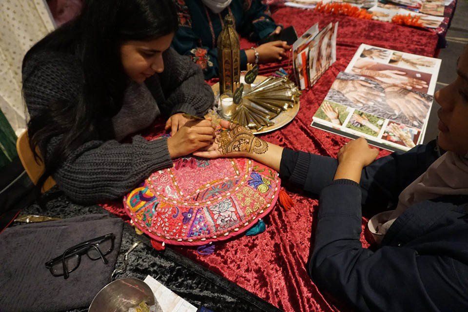 A woman is sitting at a table getting a tattoo on her hand.