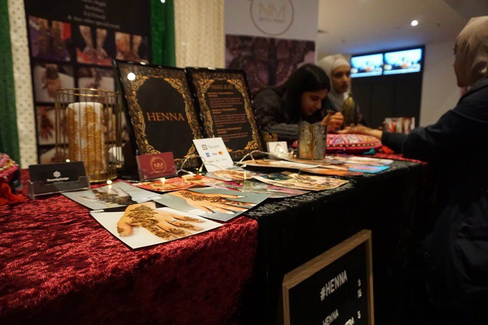 A woman is sitting at a table with a sign that says henna on it.