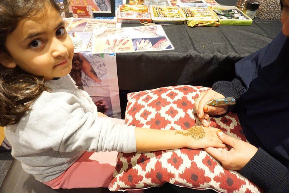 A little girl is getting a henna tattoo on her hand