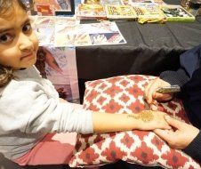 A little girl is getting a henna tattoo on her hand.
