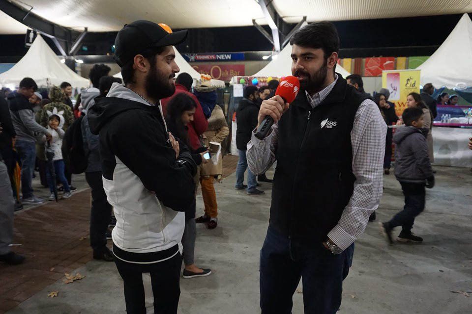 A man with a beard is holding a microphone and talking to another man.