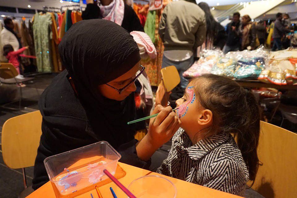 A woman is painting a little girl 's face with a brush