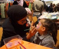 A woman is painting a little girl 's face at a table.