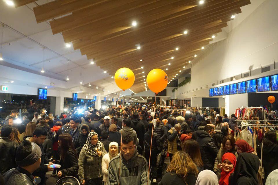 A large crowd of people are gathered in a room with balloons hanging from the ceiling.