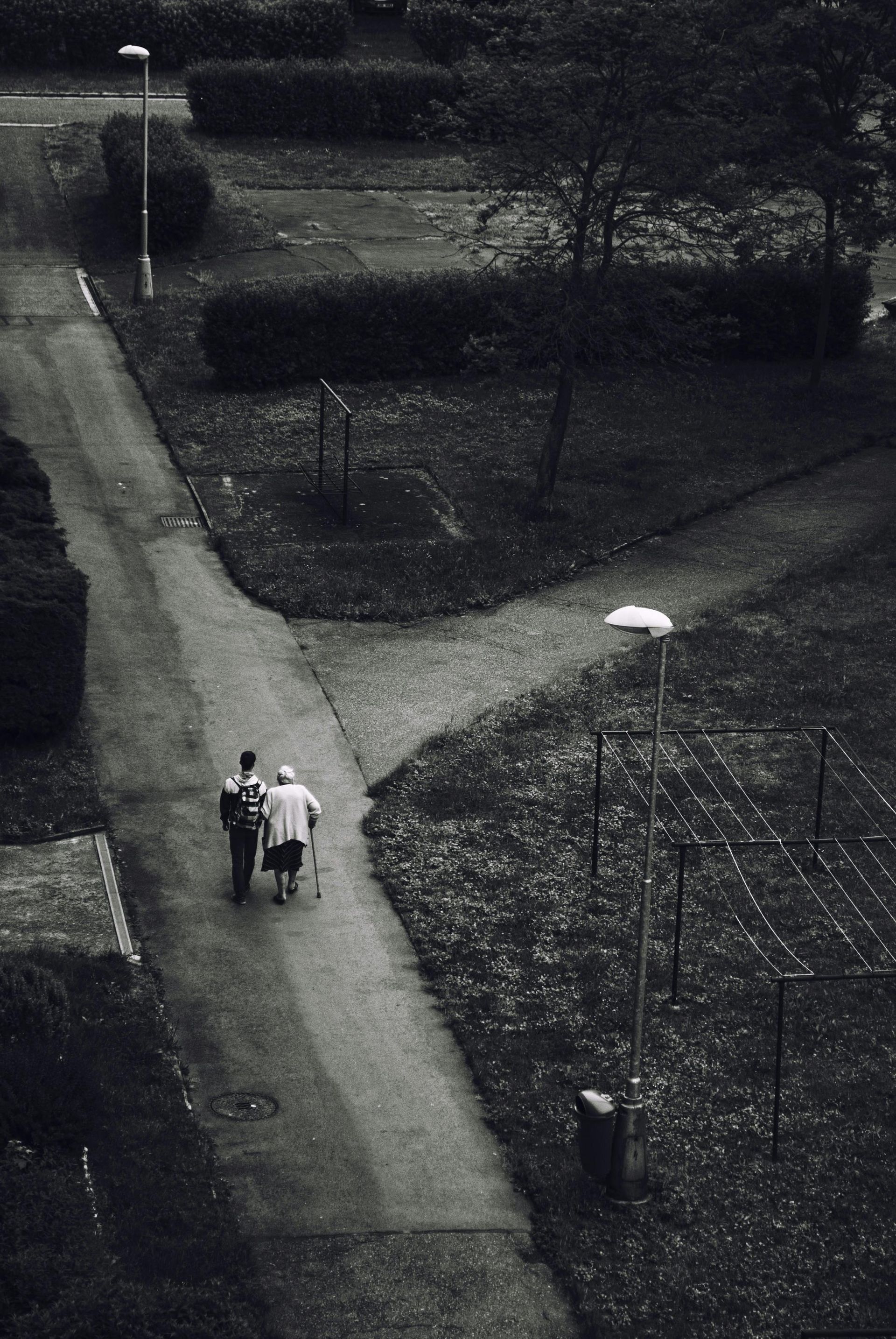 A black and white photo of two people walking down a path.