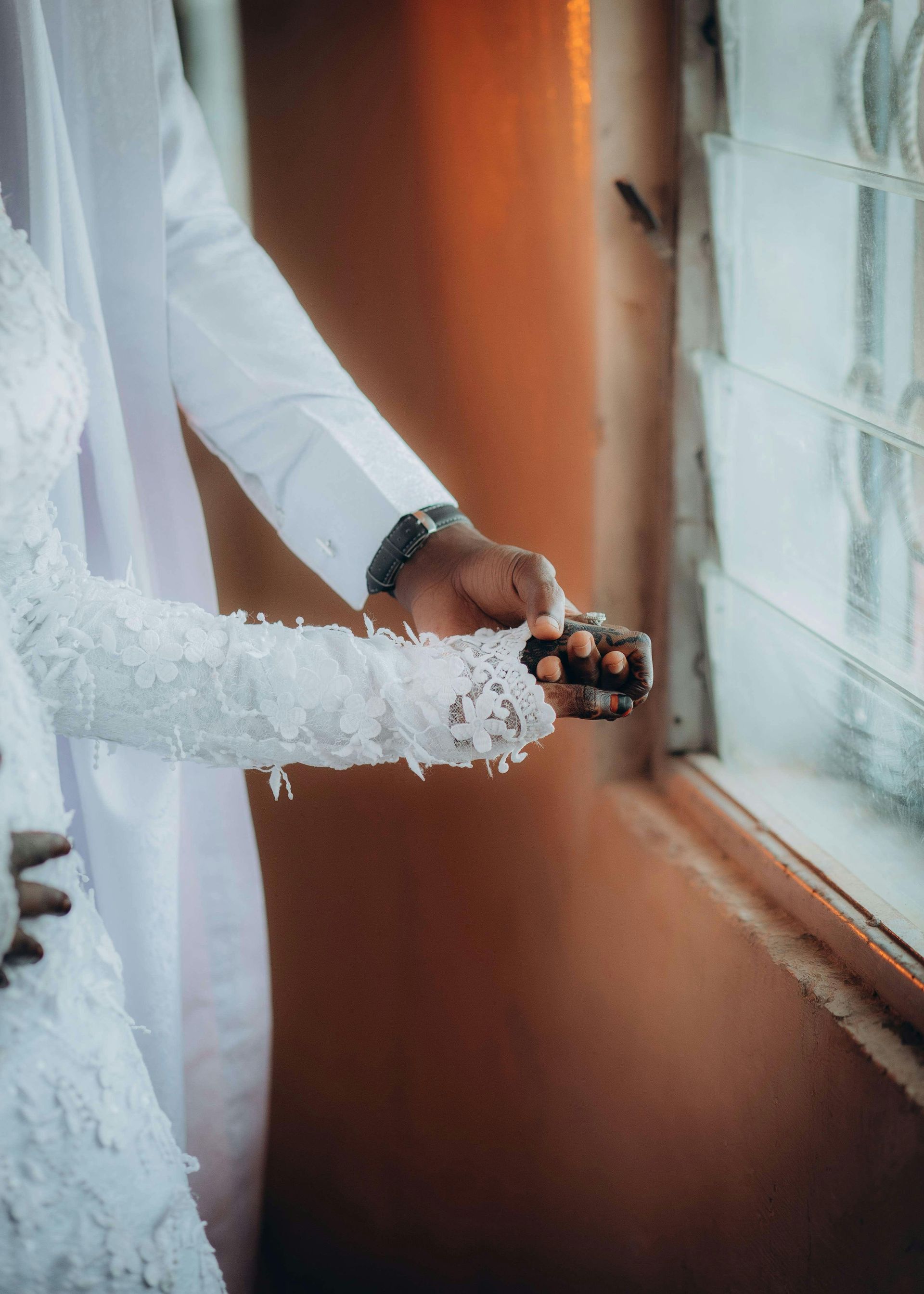 A bride and groom are holding hands in front of a window.