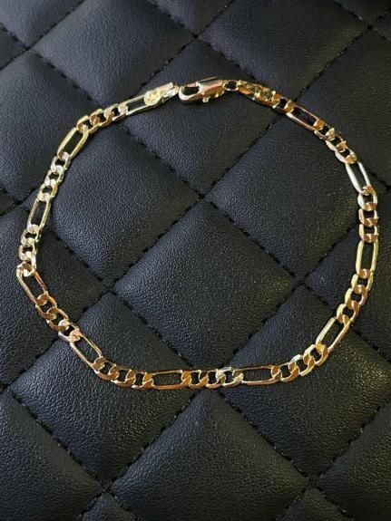 Pulsera de cadena figaro dorada sobre fondo acolchado negro.